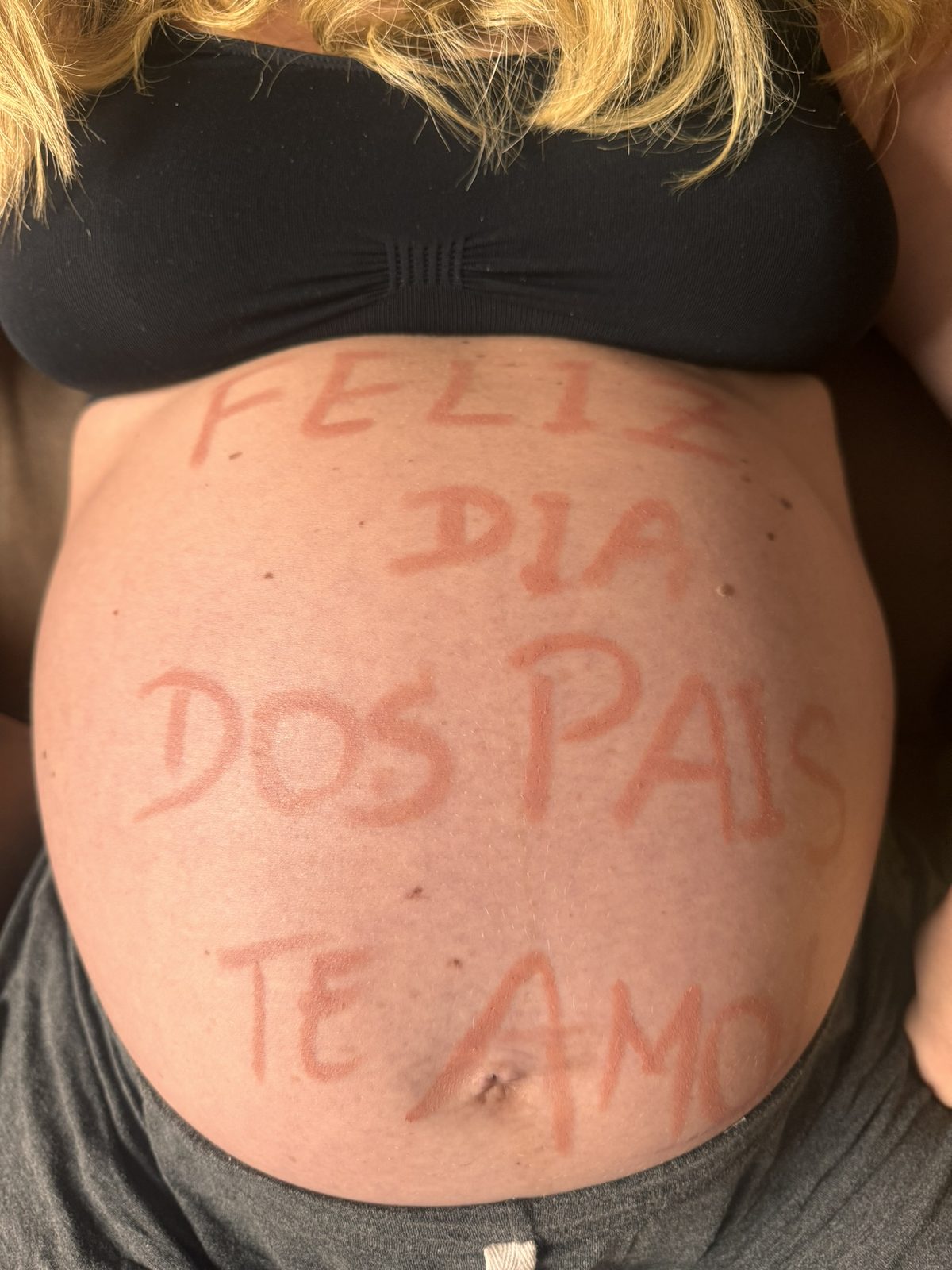 Barriga de grávida com a frase Feliz Dia dos Pais, te amo, escrita à mão.